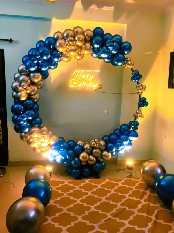 A circular metallic blue and gold balloon arch with a "Happy Birthday" neon sign for a birthday celebration.
