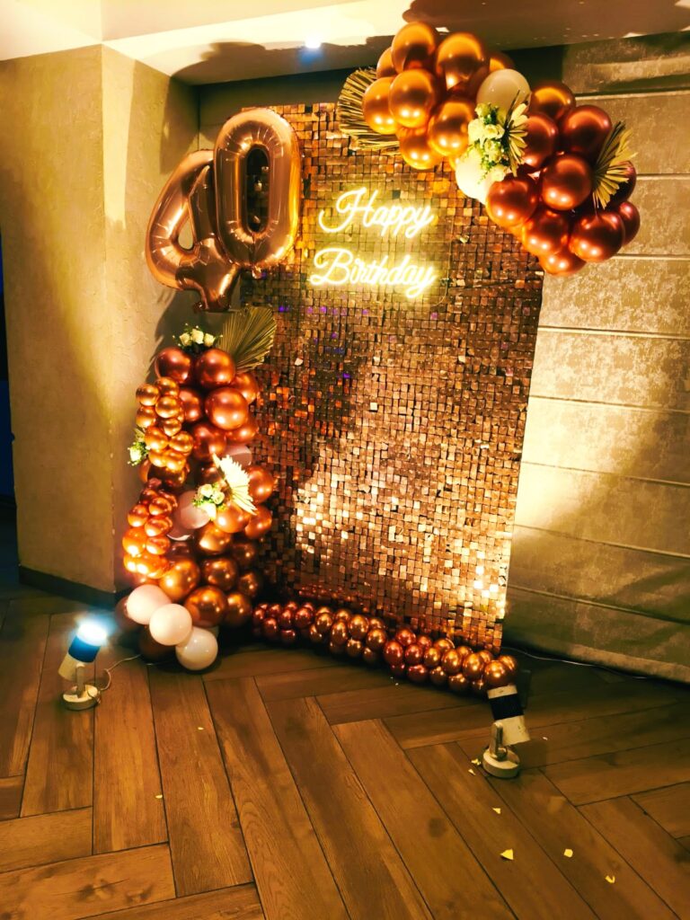 Elegant 40th birthday decoration in Jaipur with a rose gold sequin wall, neon sign, and a large metallic balloon arch by Manhagift.