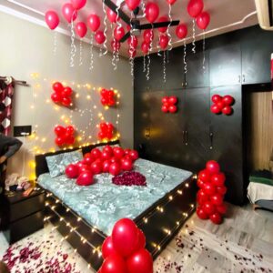 Romantic red balloon love room decoration in Jaipur with ceiling balloons, fairy lights, rose petals, and premium bedroom styling.
